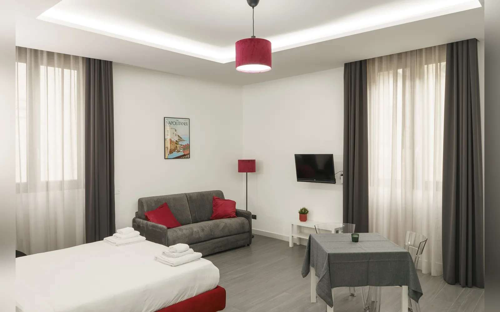 Il monolocale dall’ingresso: letto rosso, divano e tavolo davanti alla finestra