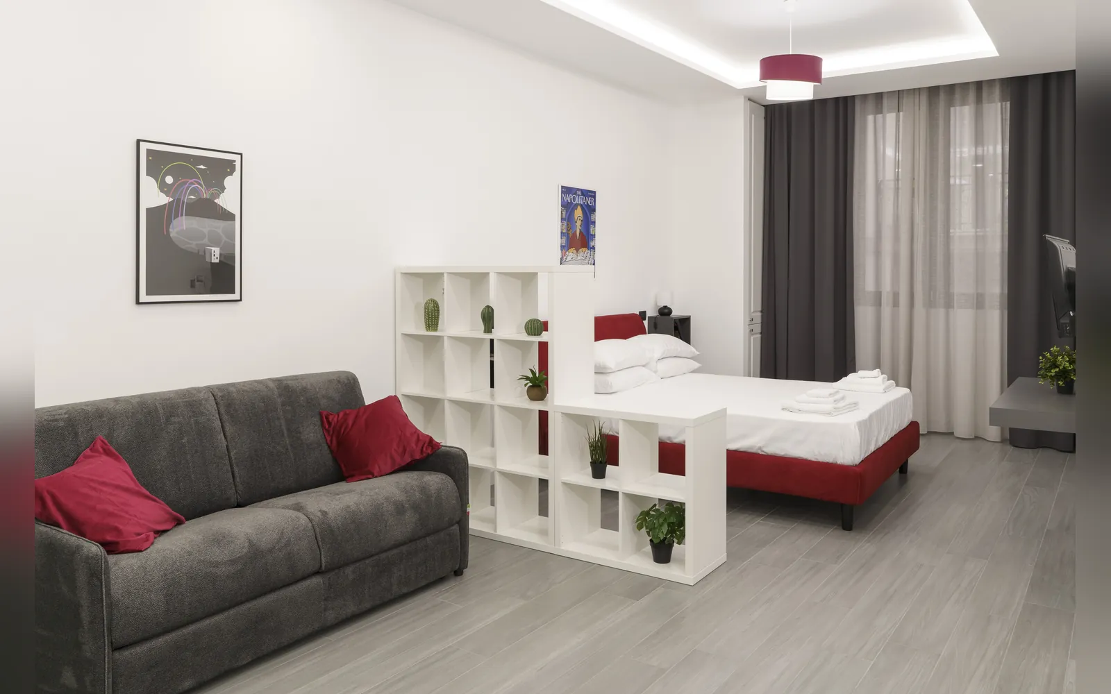 Il divano con i cuscini rossi, la libreria divisoria e il letto